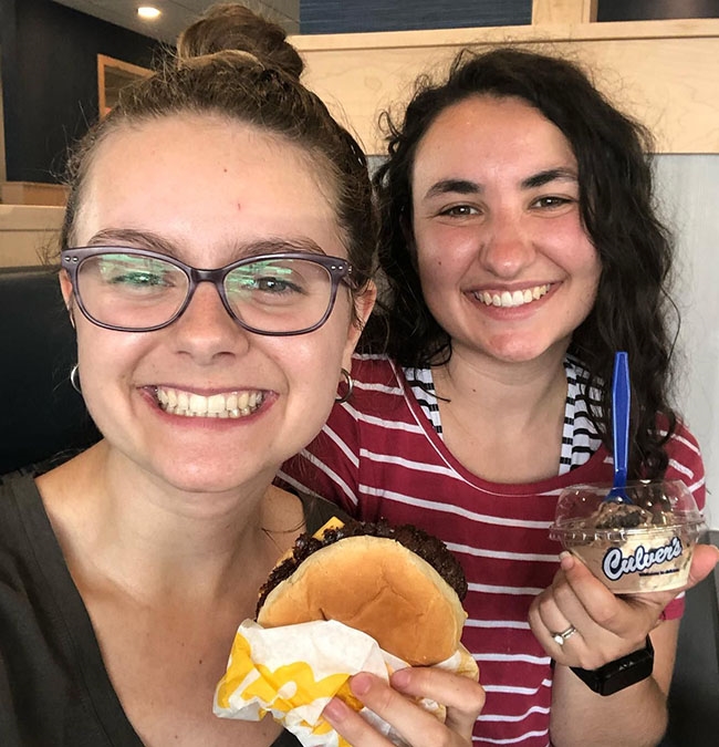 Two smiling women hold a ButterBurger and a Fresh Frozen Custard treat. 