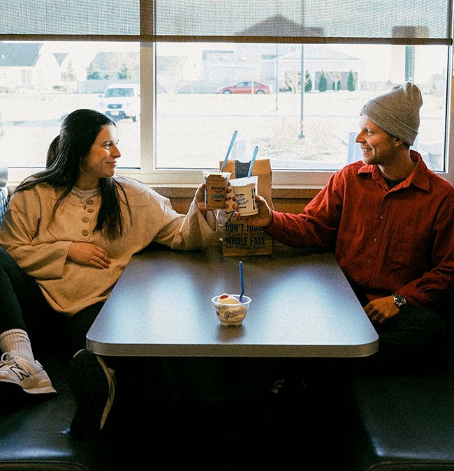 A woman and a man hold up their Fresh Frozen Custard desserts in a Culver’s booth. 