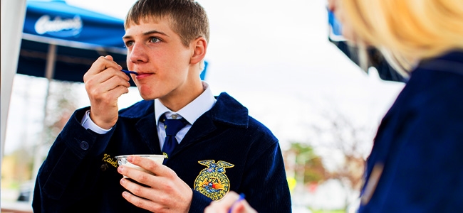 FFA student wearing a blue jacket eating a scoop of Vanilla Fresh Frozen Custard outside a Culver's