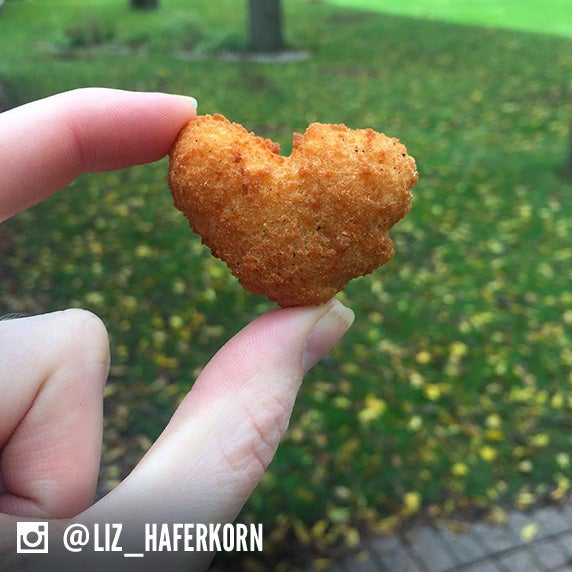 Culver’s guest holding a Cheese Curd heart with green grass and trees in the background. 