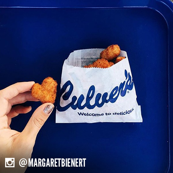 Culver’s guest holding a Cheese Curd heart alongside a bag full of Culver’s Wisconsin Cheese Curds.