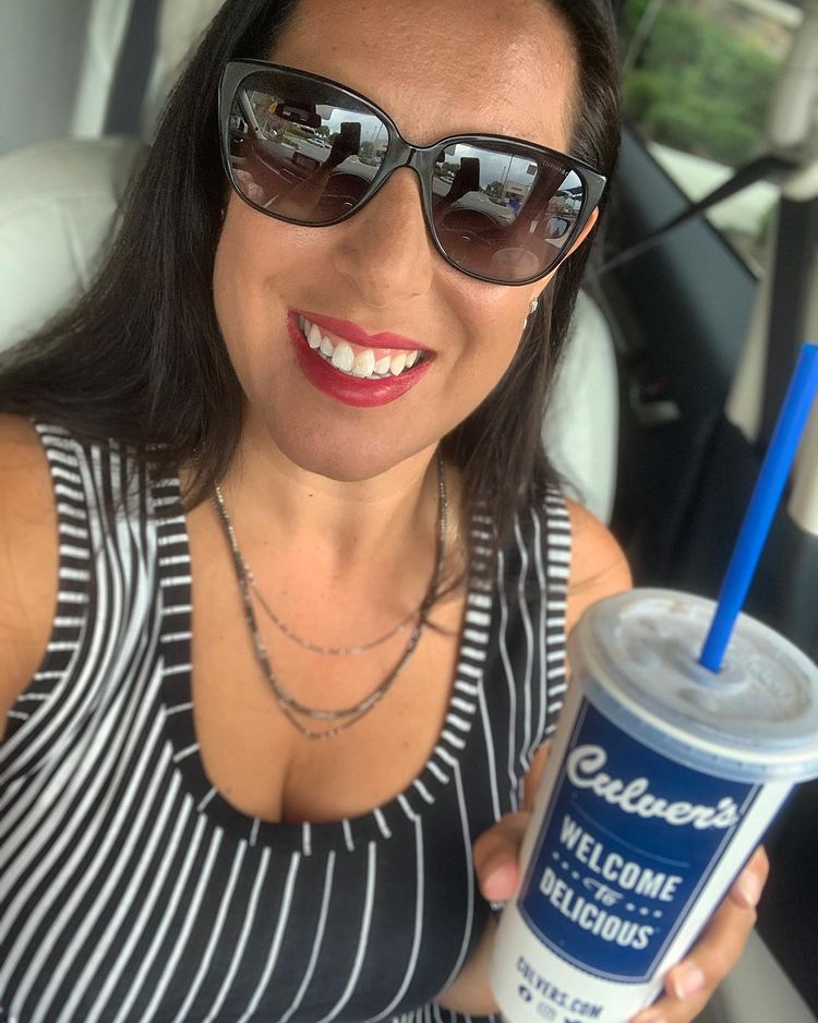 Woman wearing sunglasses and dress in her car in a Culver's drive-thru
