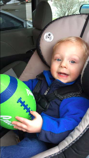 A toddler smiling in a car seat while holding a green Culver’s football