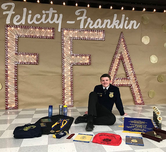 Luke poses in front of an FFA sign with a collection of FFA memorabilia.