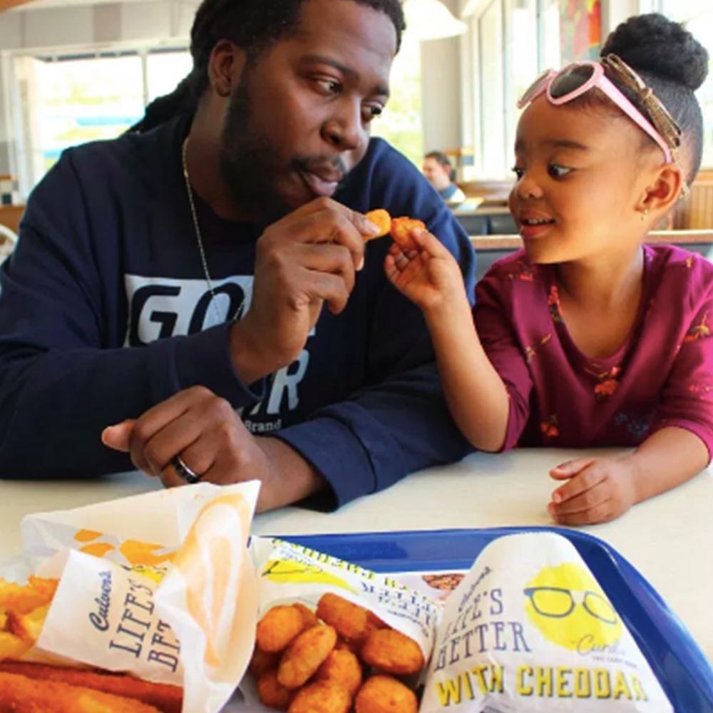 A father and daughter cheers-ing cheese curds at a Culver's