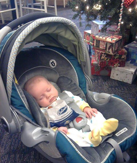 Baby Hanalei sleeps next to an order of Cheese Curds in a carrier at Culver’s and a Christmas tree in the background.