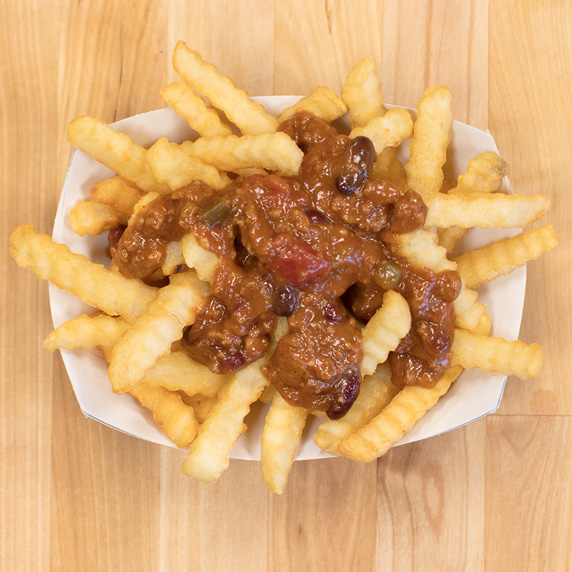 George’s Chili layered on top of Culver’s Crinkle Cut Fries in a paper tray on a wooden table