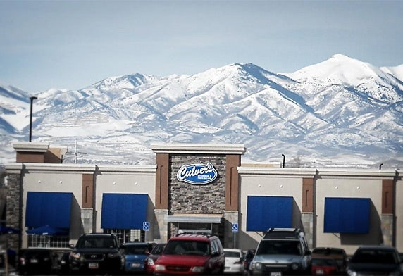 A photo of a Culver’s restaurant taken from its parking lot with snowy mountaintops in the background