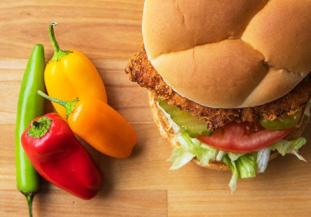 Link to story: Test Your Pepper Knowledge.The Spicy Crispy Chicken Sandwich sits next to four peppers on a wood table. 