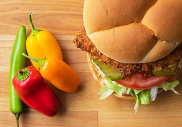 Link to story: Test Your Pepper Knowledge.The Spicy Crispy Chicken Sandwich sits next to four peppers on a wood table. 
