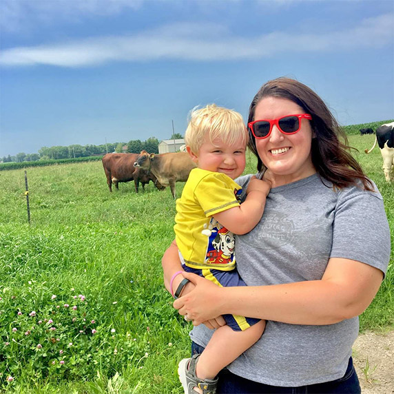 Carrie Mess holds her son while standing near her cows in a field