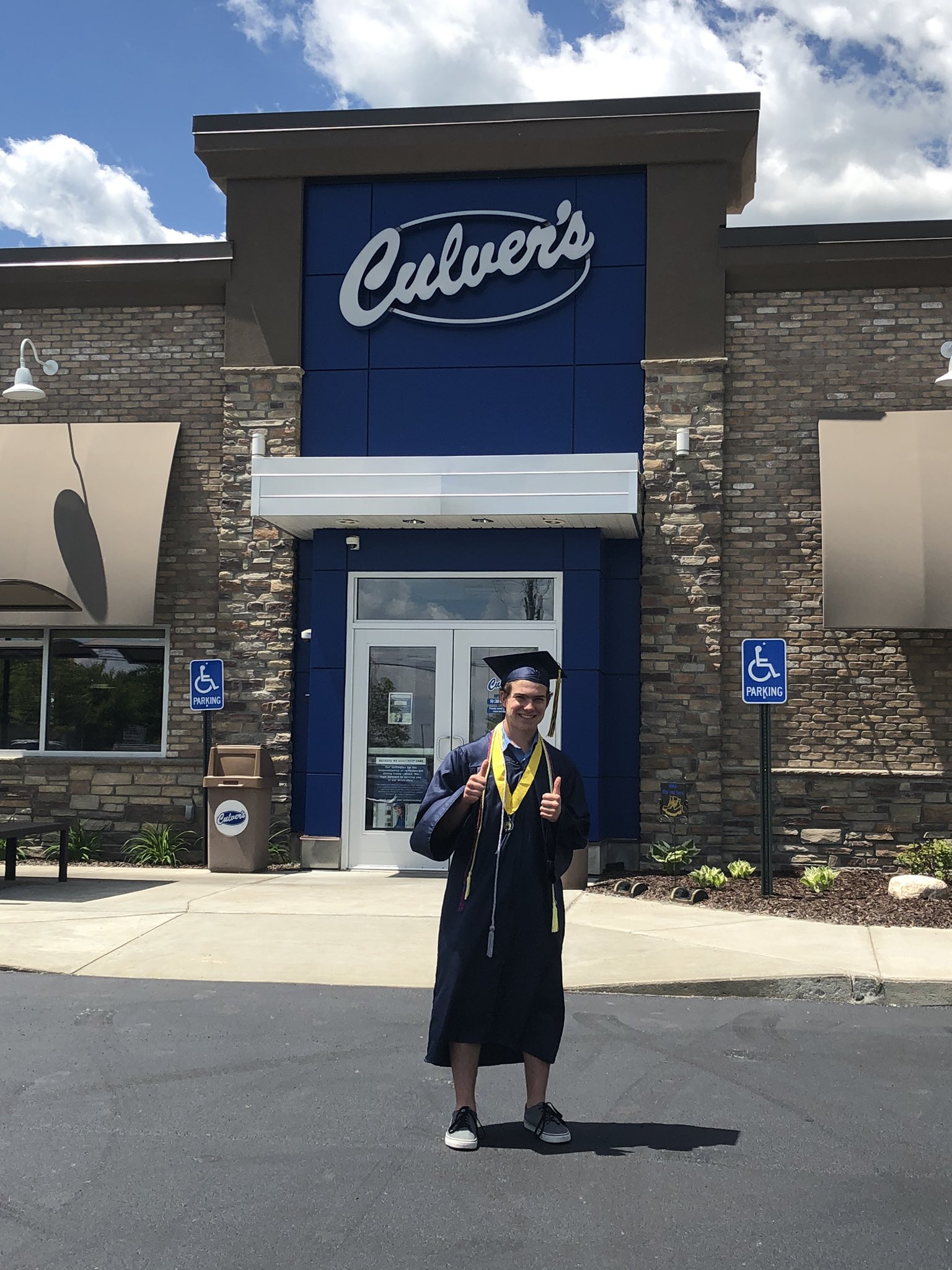 Man wearing graduation gown, standing in front of a Culver's restaurant
