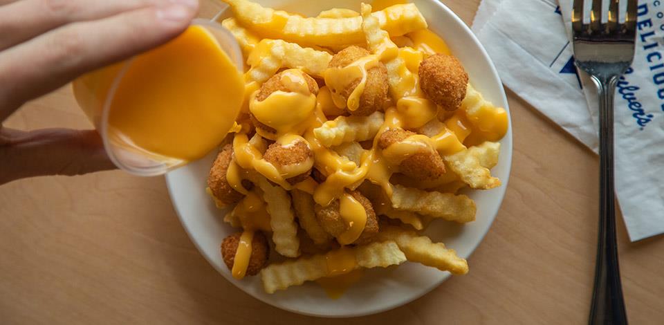 person drizzles cheese sauce over a container of crinkle cut fries and cheese curds