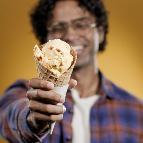 Man holds Pumpkin Pecan Flavor of the Day in a waffle cone. 