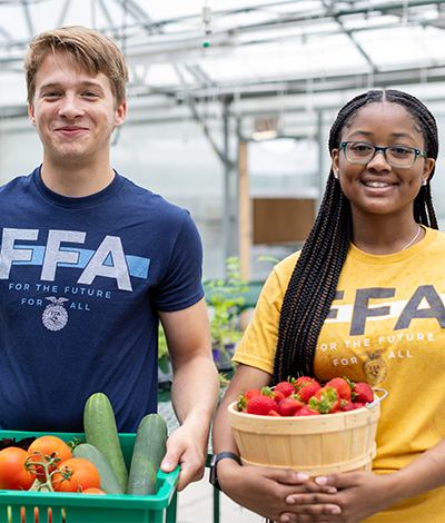 Two FFA members smile and hold baskets of produce.