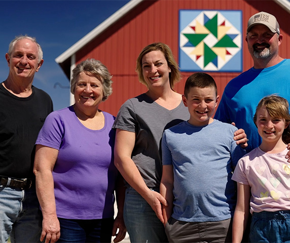 Family stands in front of red barn.
