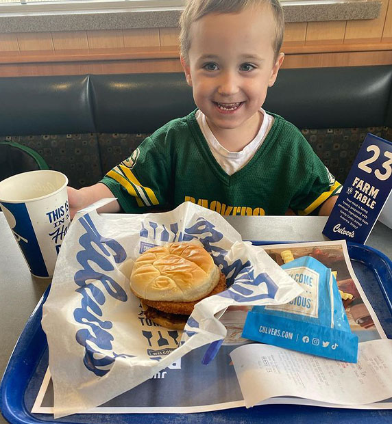Child smiling in a booth with his CurderBurger. 