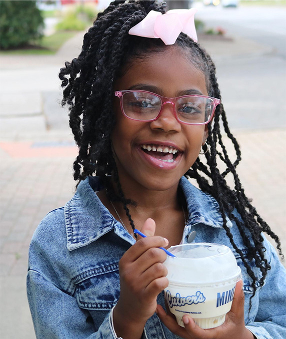 Girl holds a dish of Fresh Frozen Custard and smiles.