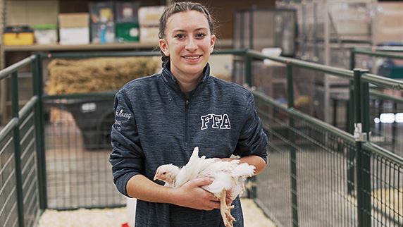Waupun FFA member and officer Samantha stands in a pen holding a chicken