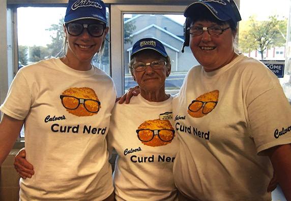 Sharon stands in the restaurant with two team members, wearing Curd Nerd shirts.