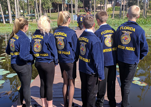 A group of FFA members stand on a dock with their backs to the camera, showing off their blue jackets