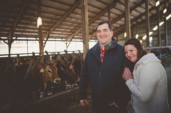 Marie and Rick pose with cows in a barn.