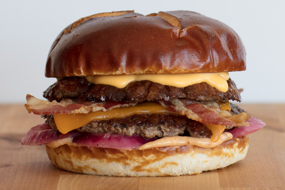 The Pretzel Haus Pub Burger sits on a wood board in front of a white background