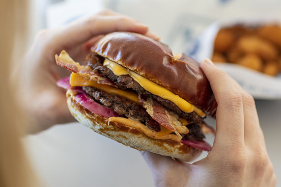 Two hands hold the Pretzel Haus Pub Burger