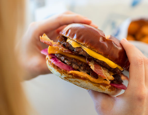 A woman holds a Pretzel Haus Pub Burger, preparing to take a bite.