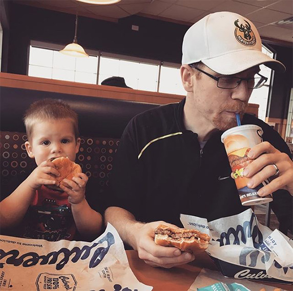 Young boy eating Culver’s ButterBurger® next to father who has a ButterBurger® in his hand and is sipping his drink