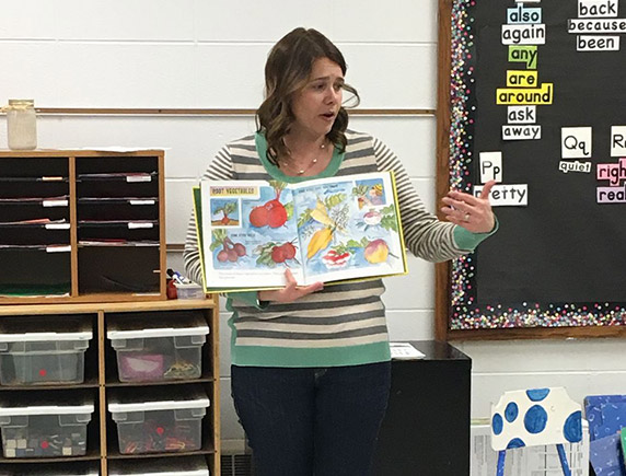 Katie Pratt hold a book in front of a classroom. 