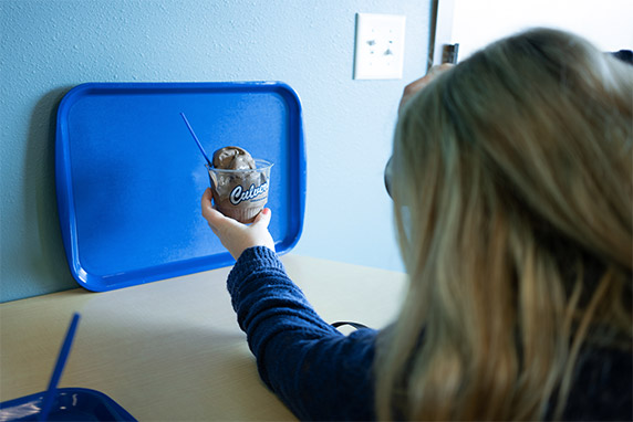 Woman holds a dish of Culver’s Fresh Frozen Custard up against a blue tray to take a photo.