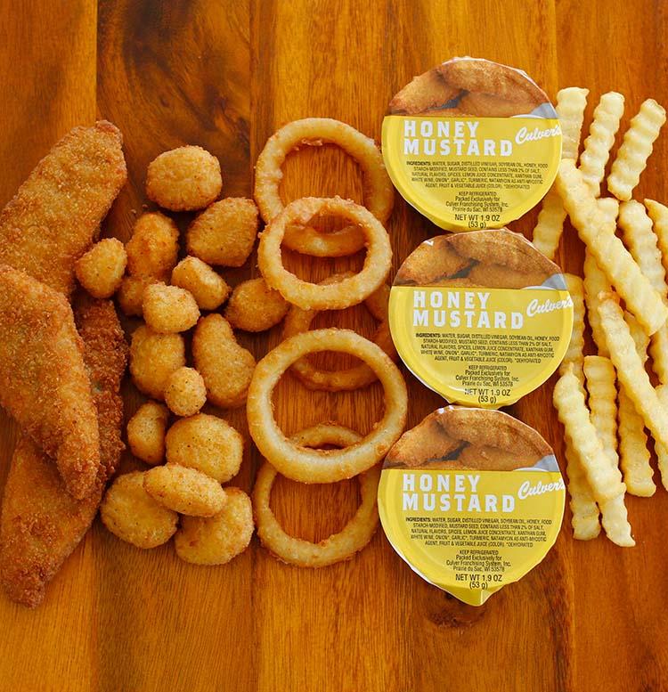 Cheese Curds, Chicken Tenders, Onion Rings, Honey Mustard Sauce and Crinkle Cut Fries on a table.