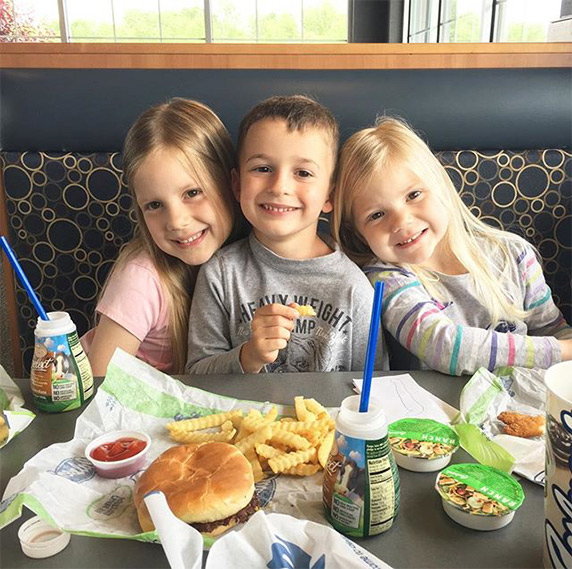 Three kids sitting in Culver’s restaurant booth eating ButterBurger® and kids’ meals