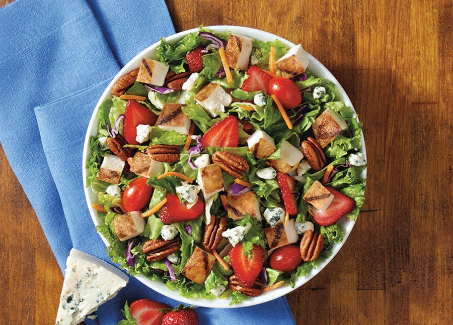 A refreshing strawberry fields salad plated on a wooden table