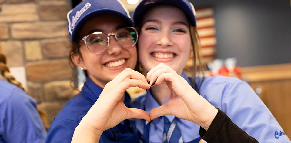 Two team members smiling and creating a heart with their hands.