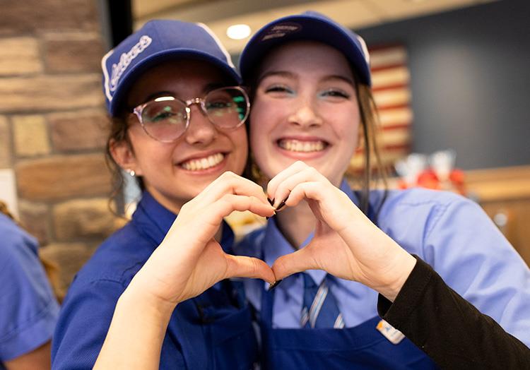 Two team members smiling and creating a heart with their hands.