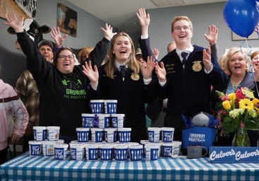 a group of people celebrate behind a table full of Culver's fresh frozen custard pints