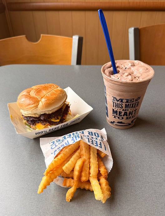 Culver’s Deluxe Value Basket sitting on a table with Crinkle Cut Fries next to a Chocolate Concrete Mixer with marshmallow and brownie pieces