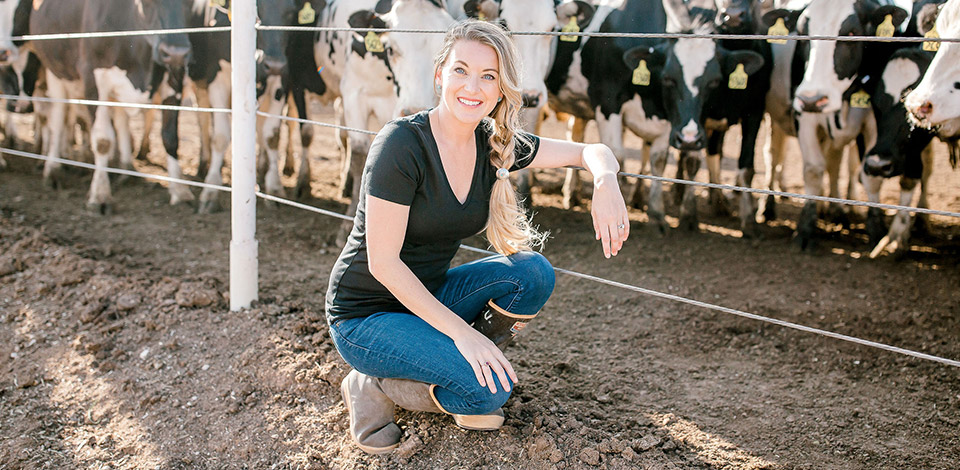 Tara Vander Dussen kneels in front of a herd of dairy cows.