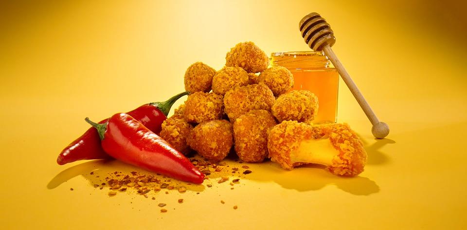 Hot Honey Curds sit in between hot peppers and a jar of honey.