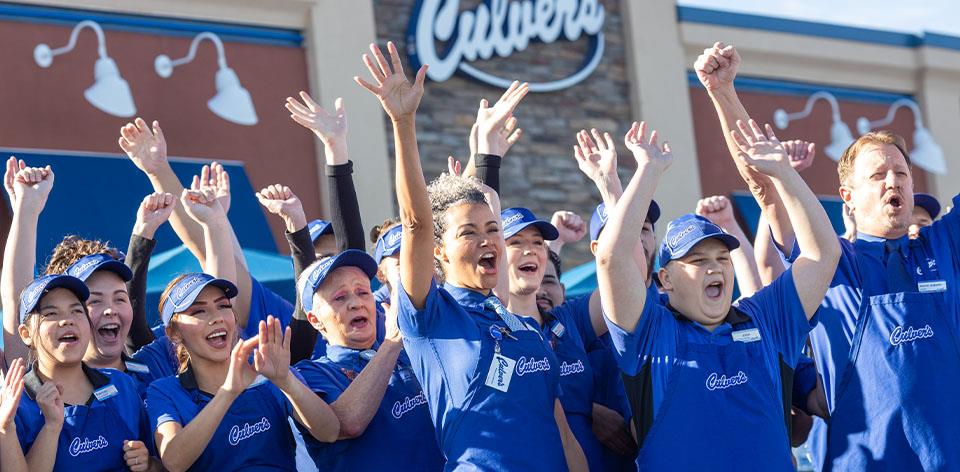 Cheering True Blue Crew members stand in front of Culver’s restaurant.