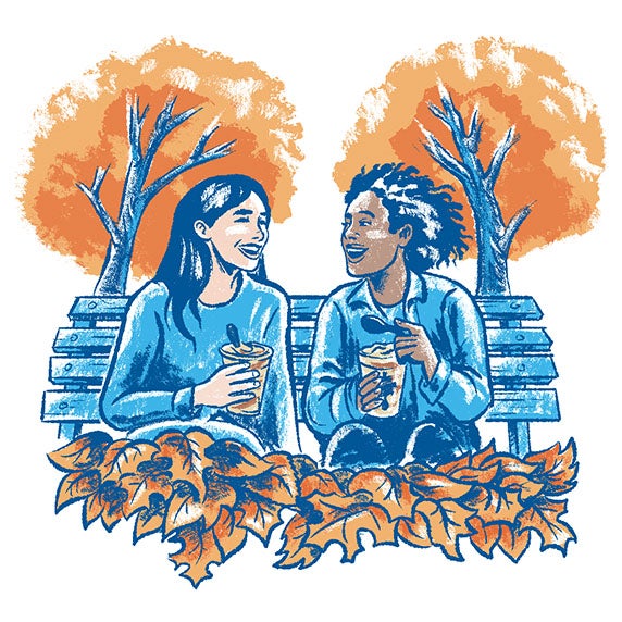 Two people enjoying Pumpkin Spice Shakes on a bench surrounded by leaves.