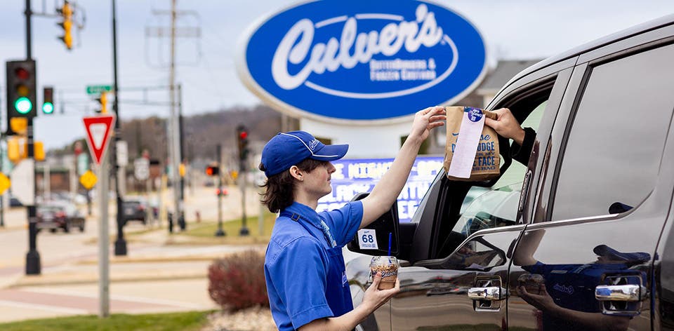 True Blue Crew member bringing a guest their order from the drive-thru in front of Culver’s sign