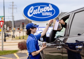True Blue Crew member bringing a guest their order from the drive-thru in front of Culver’s sign