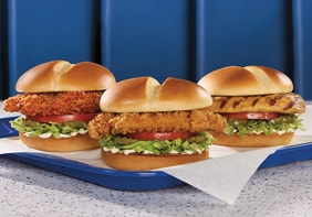 three chicken sandwiches of different styles on a tray on a table of a blue booth