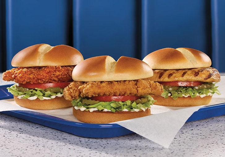 three chicken sandwiches of different styles on a tray on a table of a blue booth