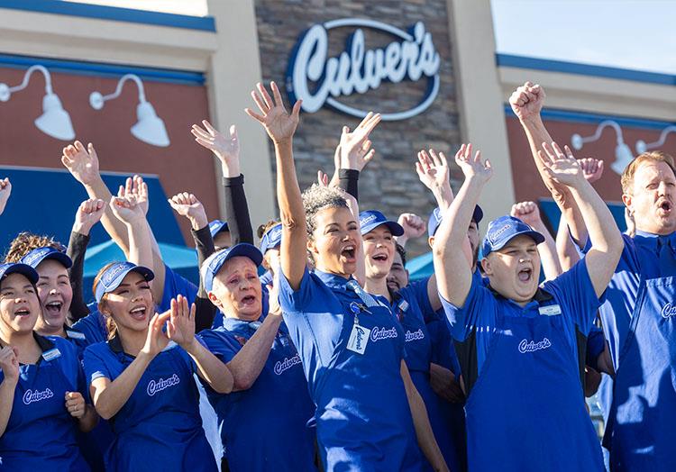 Cheering True Blue Crew members stand in front of Culver’s restaurant.