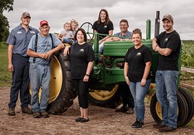 Link to story: Do you know where your food comes from? A group shot of the Feltz family, children, parents and grandparents gathered together posing in front of their green tractor.