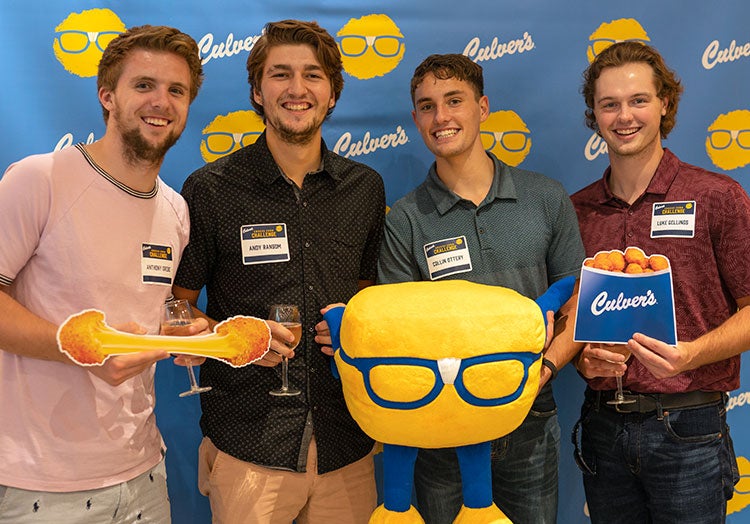 A group of young men take a photo with cheese curd props in front of a Culver’s backdrop